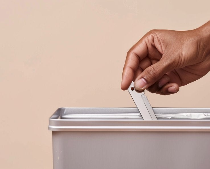 Main déposant une lame de rasoir usagée dans une poubelle métallique Handybag