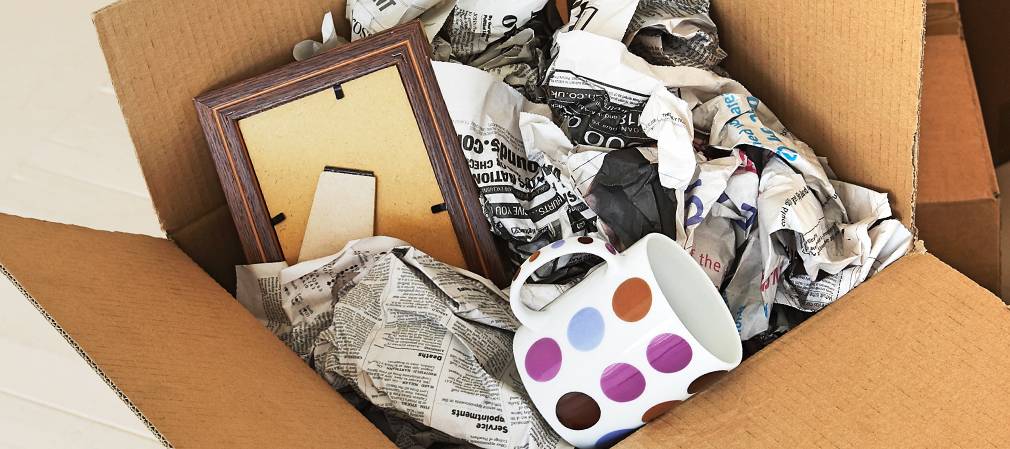 Carton d’emballage avec mug et journaux dans un décor de déménagement