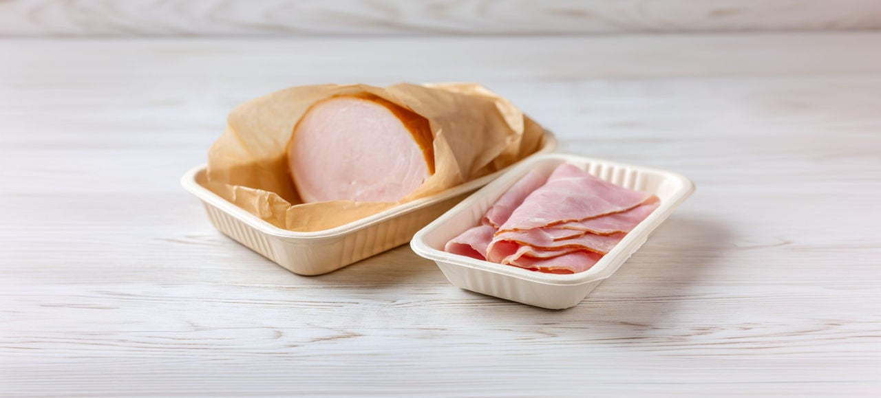 Des tranches de jambon sont présentées dans une barquette en fibre écologique, à côté d’un morceau de jambon emballé dans du papier kraft, illustrant un emballage respectueux de l’environnement pour les produits alimentaires
