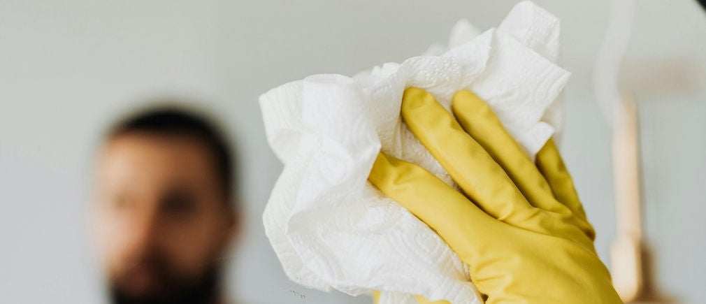 Main en gant jaune tenant un essuie tout blanc contre une vitre avec un homme flou en arrière plan