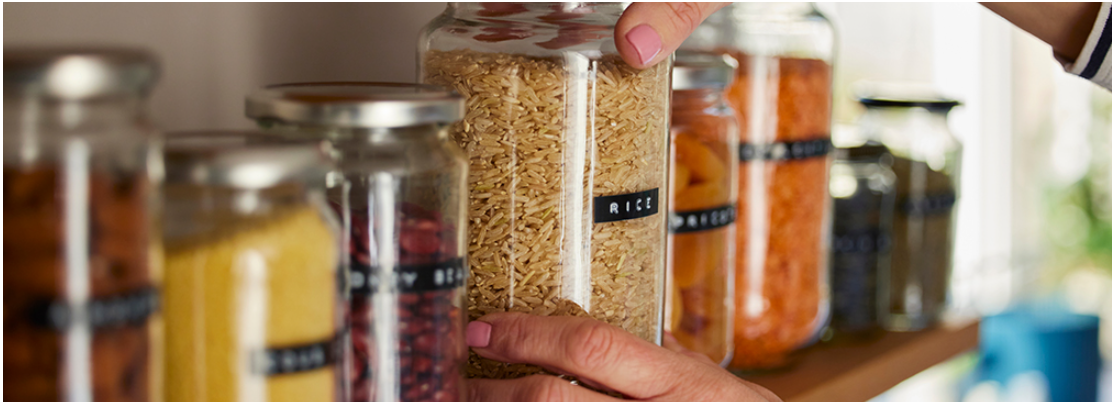 Des bocaux en verre contenant différents aliments secs, comme du riz, des légumineuses et des céréales, sont soigneusement rangés sur une étagère, illustrant une solution de conservation écologique et organisée pour la cuisine 