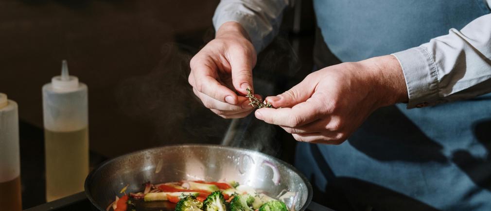 Une poêle en inox cuisant des brocolis frais avec des herbes