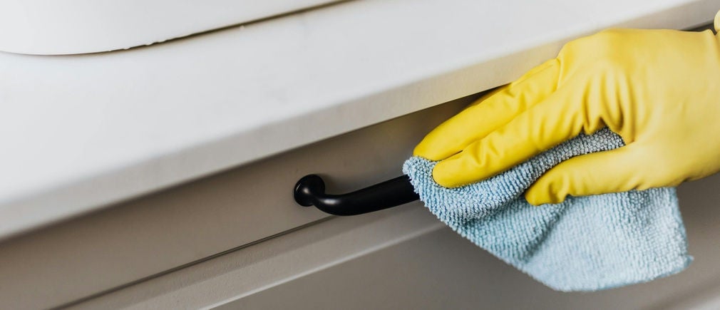 Main avec gant jaune nettoyant une poignée noire avec un chiffon microfibre bleu