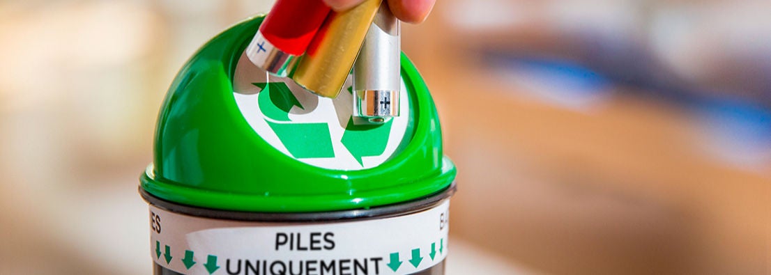 Une personne insère des piles usagées dans un conteneur de collecte spécifique pour le recyclage des piles, mettant en avant l’importance du tri des déchets dangereux 