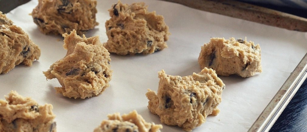 Boules de pâte à cookies crues sur papier cuisson posées sur une plaque en métal