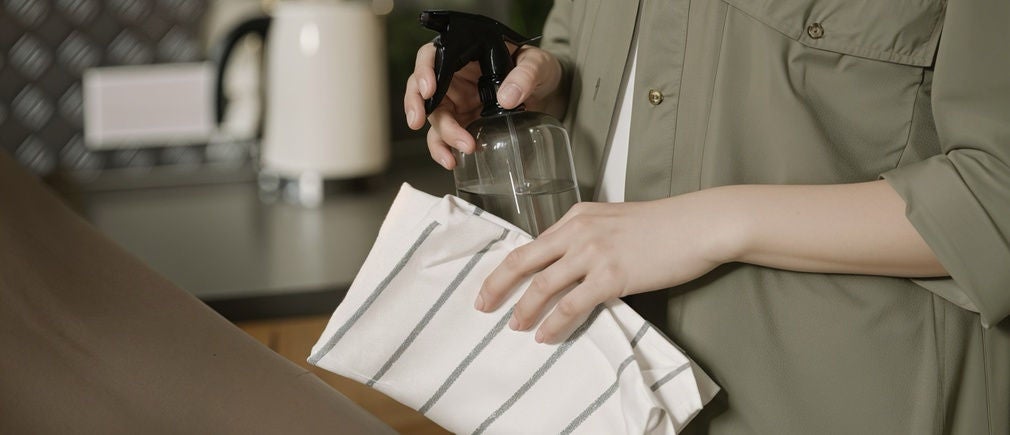 Mains nettoyant un plan de travail de cuisine avec un torchon et un vaporisateur