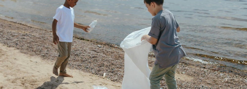 Deux enfants ramassent des dechets plastiques sur la plage au bord de l'eau