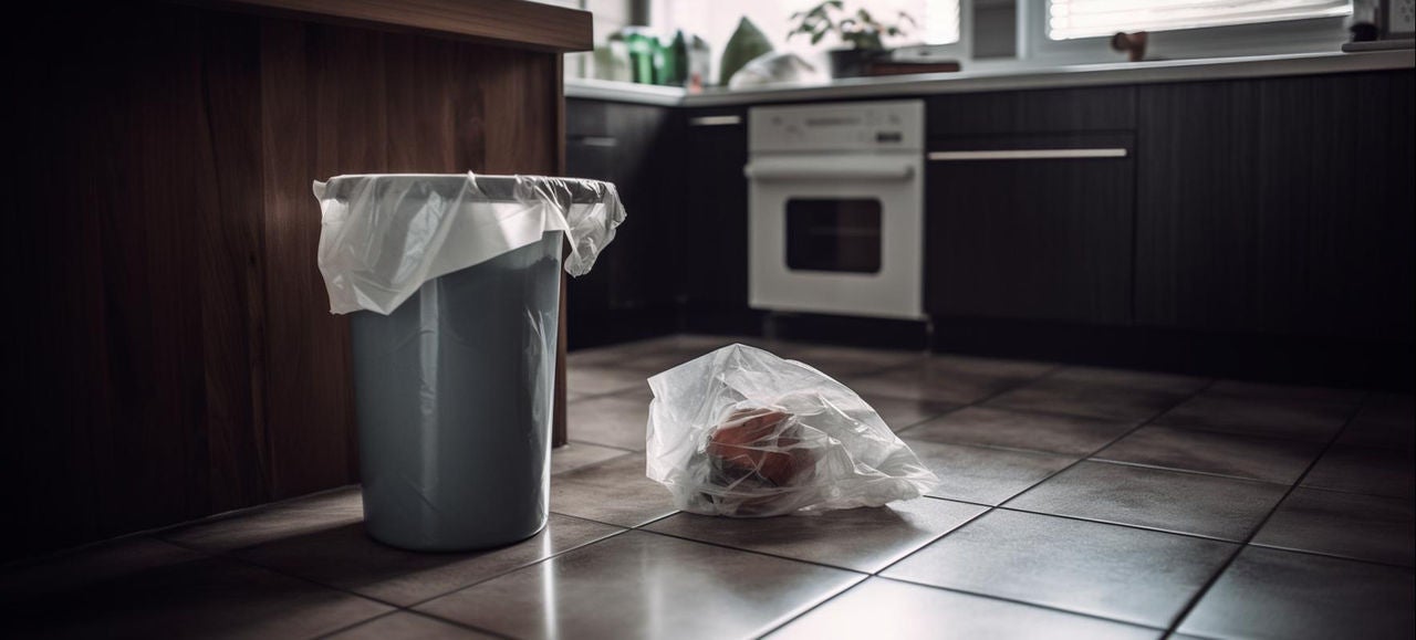 Une poubelle de cuisine équipée d’un sac poubelle est placée à côté d’un sac transparent rempli de déchets sur le sol, illustrant les techniques pour éviter les fuites et garder la cuisine propre