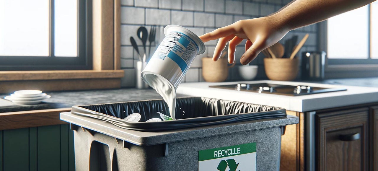 Une main dépose un pot de yaourt vide dans une poubelle de tri sélectif, illustrant le geste de recyclage des emballages alimentaires dans une cuisine moderne 