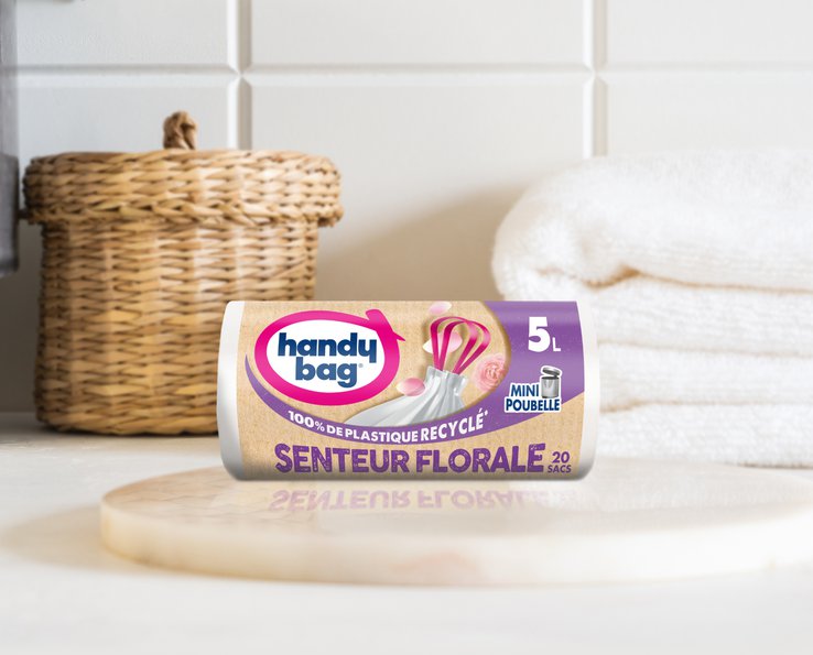 Rouleau de sac poubelle Handybag senteur florale 5 litres posé à côté de serviettes blanches
